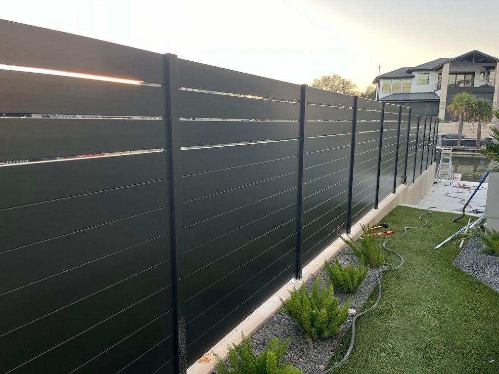 Black horizontal aluminum slat fence beside a narrow landscaped lawn