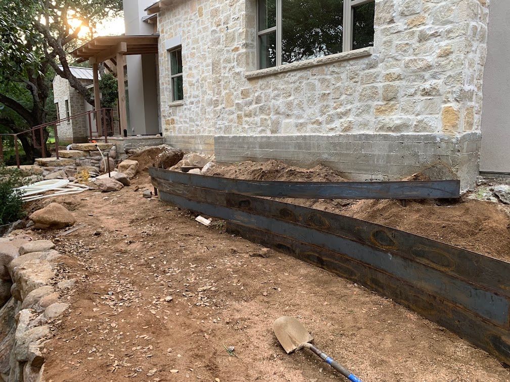 Curved metal retaining walls being installed beside a stone house