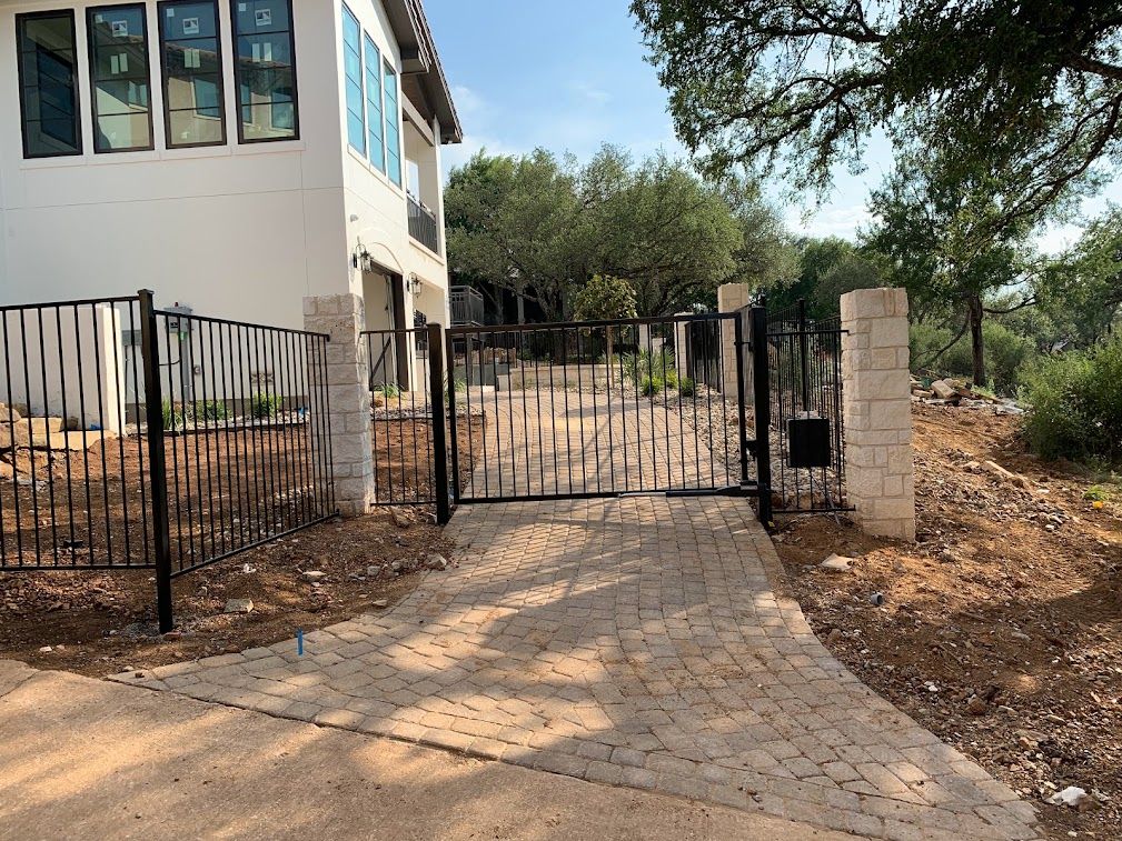 Black metal driveway gate and fencing between stone posts