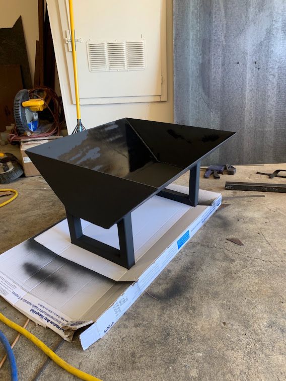 Angular black metal fire pit bowl on rectangular legs in a workshop