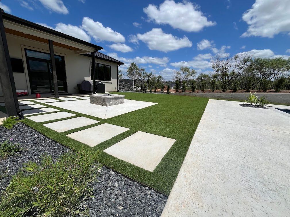 Synthetic turf lawn with pale pavers and a square patio fire pit